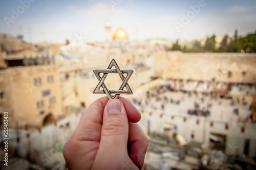 JERUSALEM, ISRAEL. February 15, 2019. Hand holding a Star of David, a Jewish religious symbol against the Western wall of the Jewish Temple in the Old city of Jerusalem. Judaism Zionism concept image.