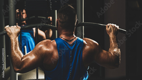 Strong male bodybuilder doing exercise for back with lat pulldown machine in gym, with color imitating social network filter