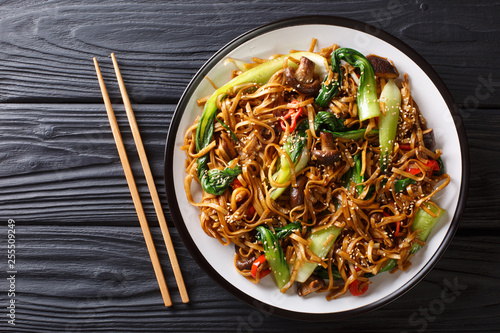 Asian vegetarian food udon noodles with baby bok choy, shiitake mushrooms, sesame and pepper close-up on a plate. horizontal top view