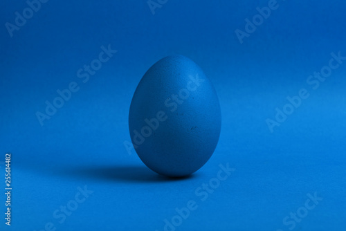 One blue painted Easter egg stand on a blue background. Happy Easter holiday card or banner. Copy space