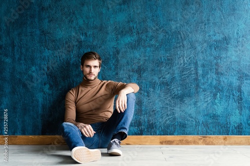 young casual fashion man sitting on the floor isolated on dark blue background.