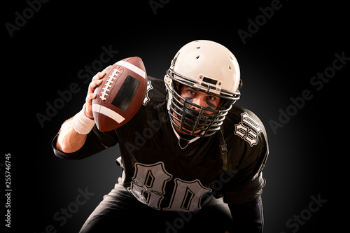 American football player in dark uniform with the ball is preparing to attack on a black background.