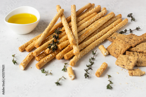 Italian grissini or salted bread sticks and multigrain crackers on a light stone background. Copy space. 