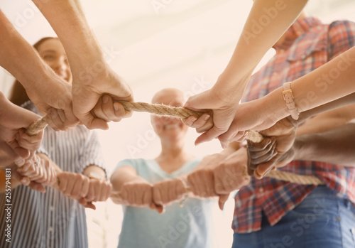 People holding rope together on light background, closeup of hands. Unity concept