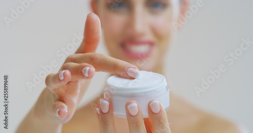 Portrait of woman with beautiful face with perfect skin just cleaned from impurities smiling and showing in camera transparent jar with day or night cream.