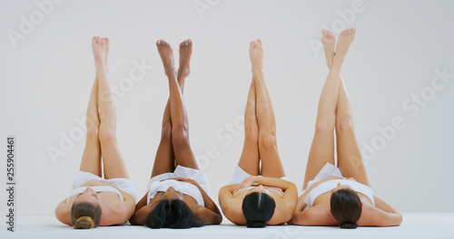 Portrait of beautiful young women of different ethnicities with perfect firm and slim bodies with hairless soft and silky legs crossed isolated on a white background.