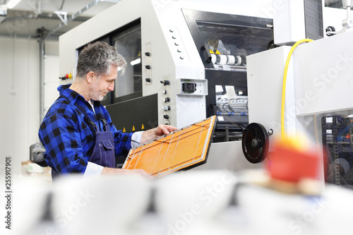 Introligatornia, mężczyzna drukarz przy maszynie montuje wykrojniki 