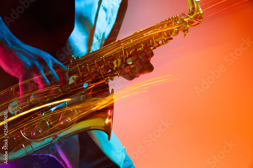 African American handsome jazz musician playing the saxophone in the studio on a neon background. Music concept. Young joyful attractive guy improvising. Close-up retro portrait.