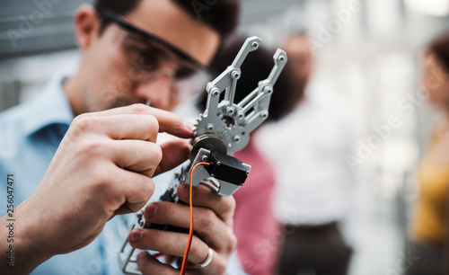 A young businessman or scientist with robotic hand standing in office, working.