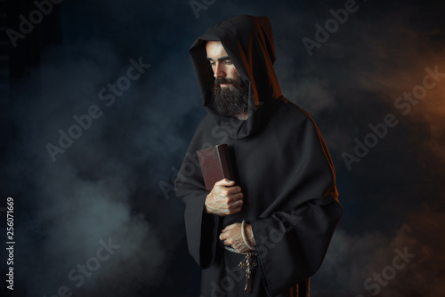 Medieval monk in robe holds spellbook in hands