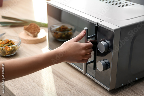 Young woman using microwave oven on table in kitchen