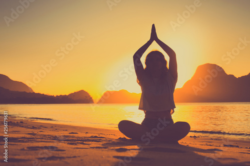 meditating woman by the ocean with rocks in the background at sunset