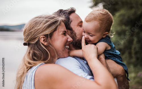 A young family with a toddler girl outdoors by the river in summer.