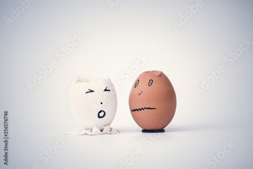 Two broken eggs in the form of human head (white and black) complain to each other. Concept.