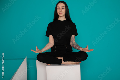 Beautiful young woman sitting in yoga position and meditating isolated over blue background 