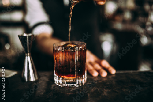 A close up shot of a bartender pouring whiskey. Classic old fashioned cocktail served with a cube of ice. Concept of bourbon whisky, spirits and alcohol.