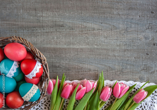 Wielkanocne tło - kosz z kolorowymi pisankami i różowe tuliapny