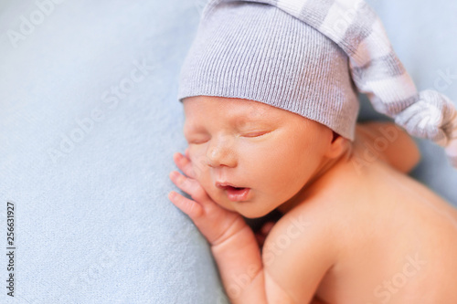 Sleeping newborn baby on the blue background. Child in a nightcap close-up portrait