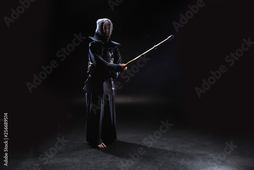 Full length view of kendo fighter in armor practicing with bamboo sword on black