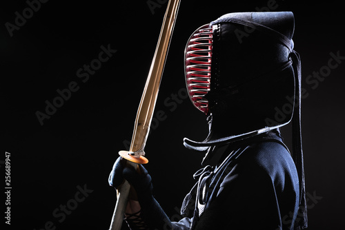 Side view of kendo fighter in traditional helmet holding bamboo sword on black