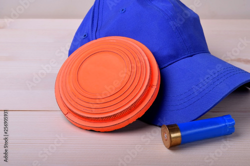 Flying target plate for shotgun sport, blue cap and a shell against the wooden background
