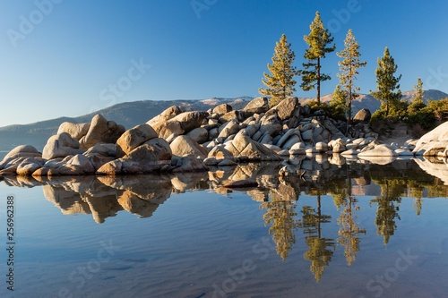 Beautiful Lake Tahoe along the shoreline at golden hour sunset with boulder rocks poking out of the blue water