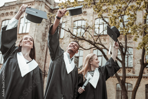 Positive delighted leavers raising their graduation hats