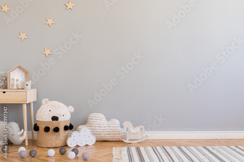 Stylish scandinavian newborn baby room with toys, children's chair, natural basket with teddy bear and small shelf. Modern interior with grey background walls, wooden parquet and stars pattern.