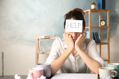Young woman with note HELP on forehead at workplace. Space for text
