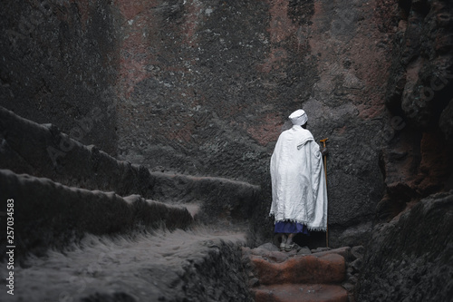 Old priest in white robe praying at a wall at the lalibela church in ethiopia 