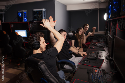 Enthusiastic e-sport gamers. Joyful young people sitting at powerful computers in gaming centre and raising hands triumphantly, celebrating victory in game.