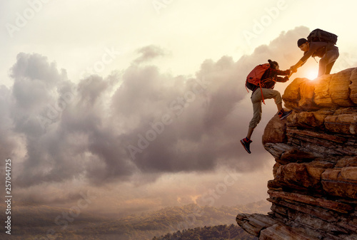 People helping each other hike up a mountain at sunrise. Giving a helping hand, and active fit lifestyle concept.Asia couple hiking help each other.