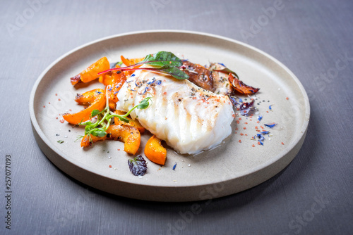 Gebratenes dänisches Skrei Kabeljau Fisch Filet mit Kürbis, Pilze und Salat als closeup auf einem Modern Design Teller