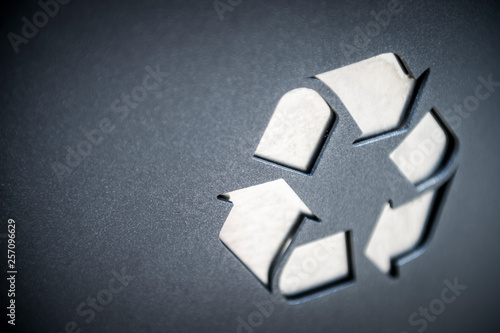 Close up of white recycling symbol in raised texture on smooth dark background