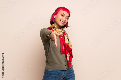 Young woman with pink hair over yellow wall shaking hands for closing a good deal