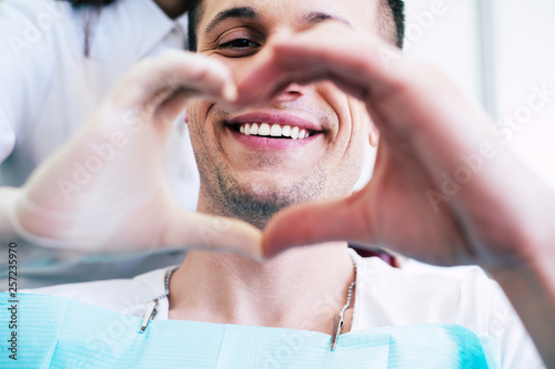 Cheer of heart. A patient with white and healthy smile in the center of a heart made from two hands of a doctor and a patient which is telling about pleasant emotions of the appointment.