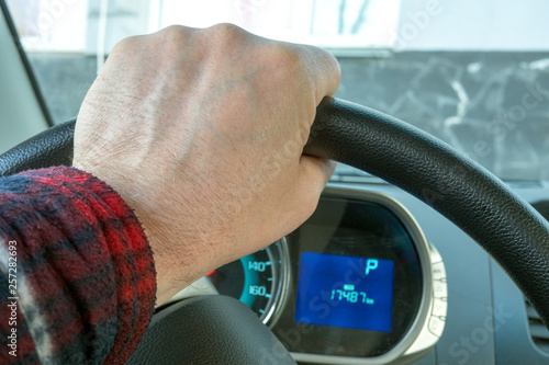 Hand of mans on the steering wheel, and Dashboard of the car, which stands still.