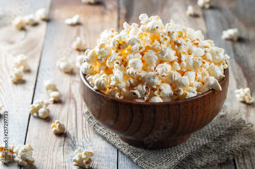 A wooden bowl of salted popcorn at the old wooden table. Dark background. selective focus