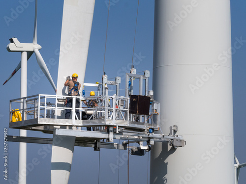 Workers on a hanging platform repair a damaged rotor blade on a wind turbine