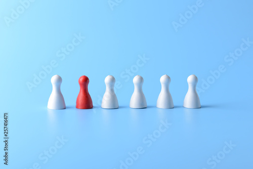 Red pawn among white ones on color background. Concept of uniqueness