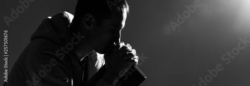 Religious young man praying to God on dark background, black and white effect