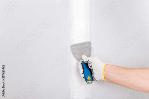 Man with putty knife shows how to hide the connection place between two pieces of dry walls using putty and construction tape