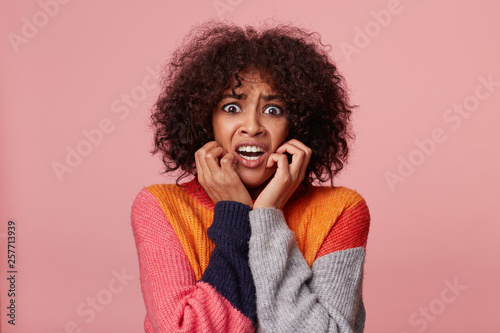 Close up portrait of scared hysterical african american girl with afro hairstyle looking frightened, in panic, nervous, scared, keeps fists near her face, isolated over pink background