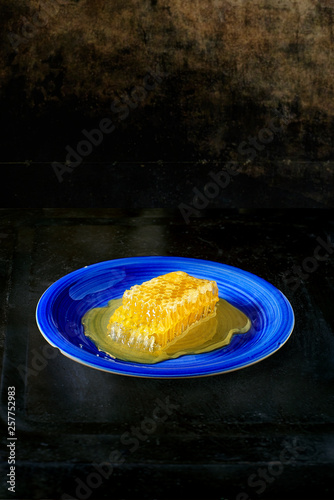 Honeycomb piece with honey on a blue plate over a metallic table.