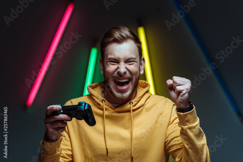 young adult handsome and screaming man looking at camera and holding gamepad