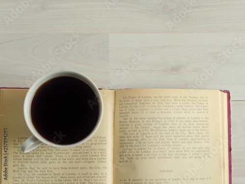 a cup of coffee and an open book on white wooden background.
