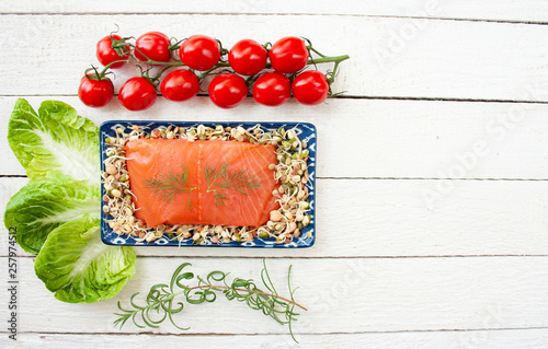 Wędzony łosoś na tacy wypełnionej kiełkami otoczony gałązkami rozmarynu, pomidorami i sałatą