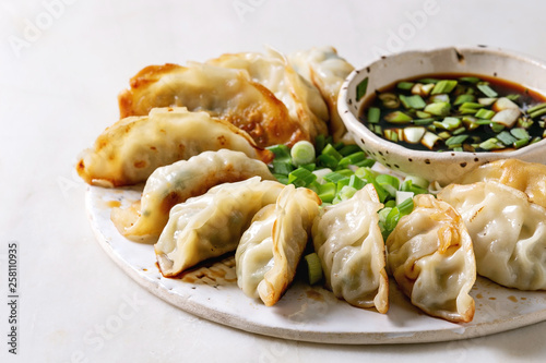 Fried asian dumplings Gyozas potstickers in white ceramic plate served with bowl of soy onion sauce over white marble table. Close up. Asian dinner