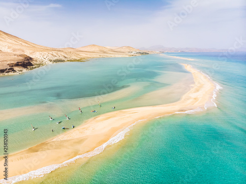Aerial view of beach in Fuerteventura island with windsurfers learning windsurfing in blue turquoise water during summer vacation holidays, Canary islands from drone