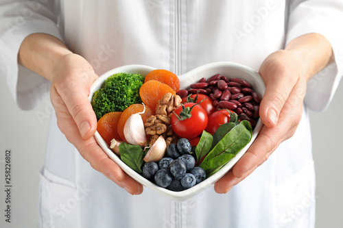 Doctor holding bowl with products for heart-healthy diet, closeup